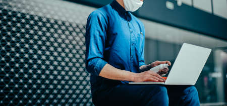 man in a protective mask spraying a bactericidal spray on the surface of a laptop.
