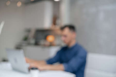 blurry image of a young man working on his laptop in the kitchen.