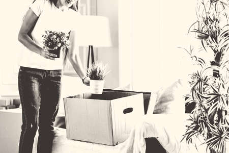 young woman takes her favorite plants out of a cardboard boxの写真素材