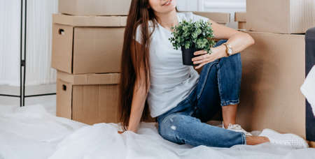 young woman with a home plant sitting on the floor in the new living room.の写真素材