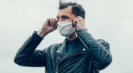 young man putting on a protective mask standing on the streetの写真素材