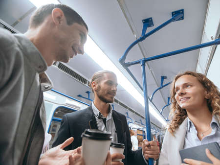 group of young people talking while standing on a subway train.の写真素材