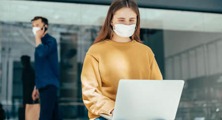 young woman in a protective mask uses her laptop on the street