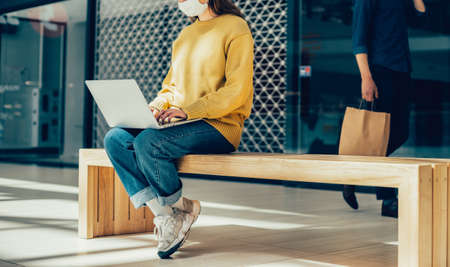 young woman is working on a laptop while sitting outside a city buildingの写真素材