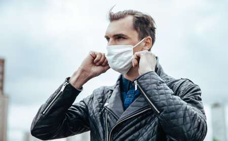 young man putting on a protective mask standing on the streetの写真素材