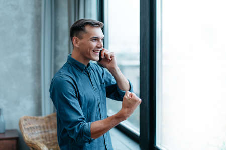 man with a smartphone, standing near the window.