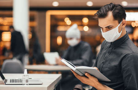 young man reading a book sitting at a table in the food courtの写真素材