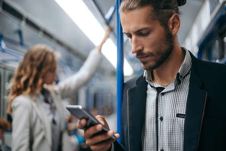 young man using his smartphone on a subway train.