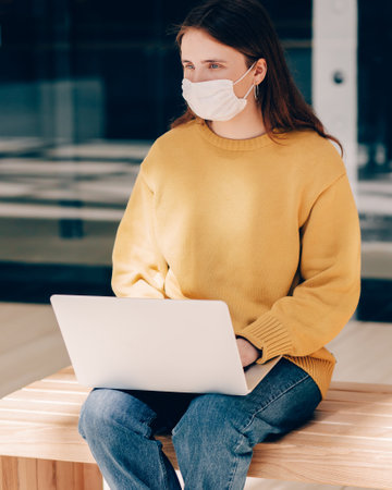 young woman in a protective mask using a laptop on a city street.の写真素材