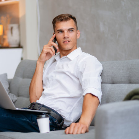 young man is talking on a smartphone, sitting on the sofa.の写真素材