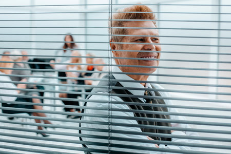 close up. cheerful office employee looking through window blinds.の写真素材