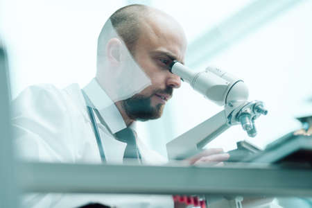 young scientist studying fluid samples through a microscope .