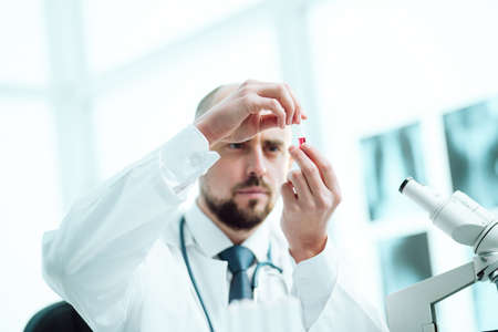 scientist with an ampoule of vaccine sitting at a laboratory table .