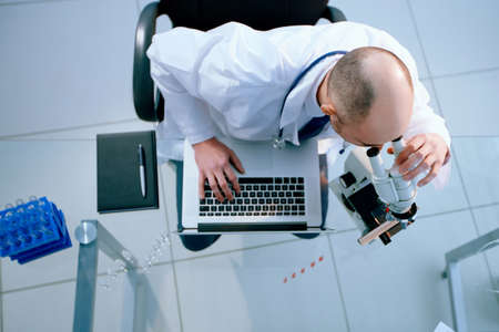 scientist looking through a microscope and using a laptop during his research.