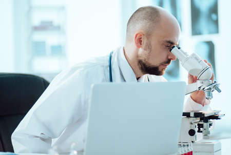 scientist works on a laptop while sitting at a table in a medical laboratory.
