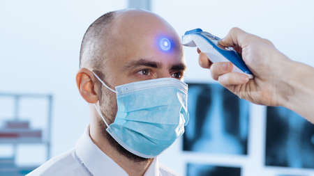 man in a protective mask is measuring the temperature with a digital thermometer.