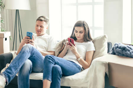 young couple with smartphones sitting on the sofa in a new apartment .の写真素材