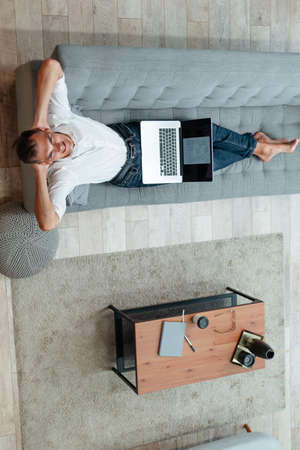 happy man with a laptop lying on the couch .