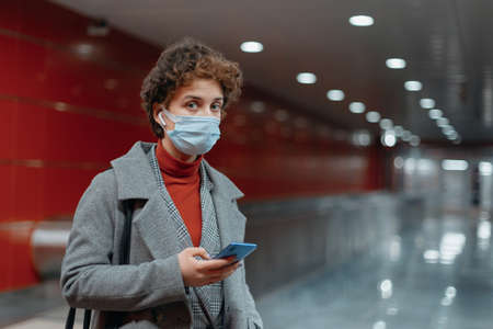 woman reading a message standing on a subway platform.