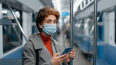 woman with headphones and a smartphone standing in a subway car .の写真素材
