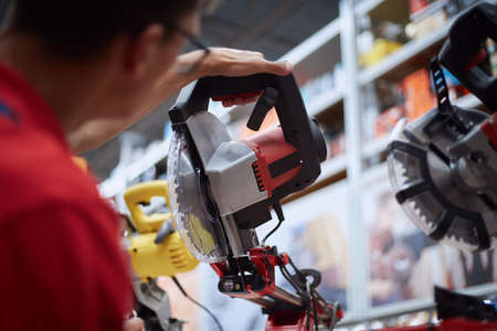 sales assistant of a construction store stands near a shelf with power tools.