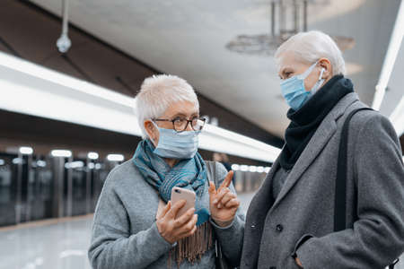 two mature women discussing something while standing on a subway platform.の写真素材
