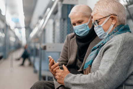 two mature women looking at a smartphone screen sitting in a subway car.