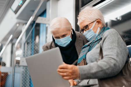 two mature women using a laptop while sitting in a subway car.の写真素材