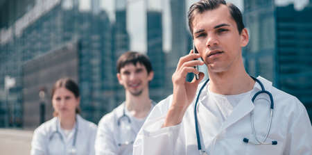doctor with a smartphone standing near a hospital building .