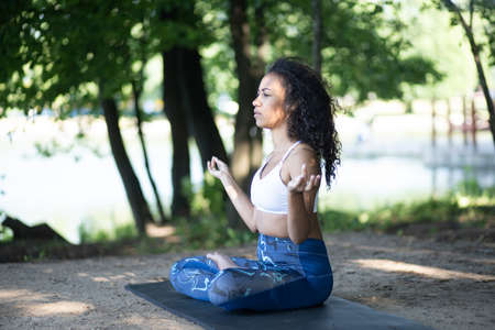 athletic young woman meditating in a city park .の写真素材