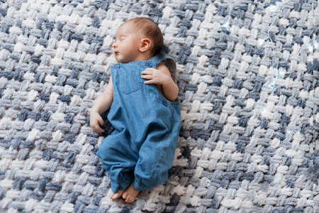 newborn baby in a blue jumpsuit lying on a knitted blanket .の写真素材