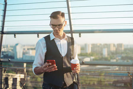 business man with a smartphone and a takeaway coffee standing onの写真素材