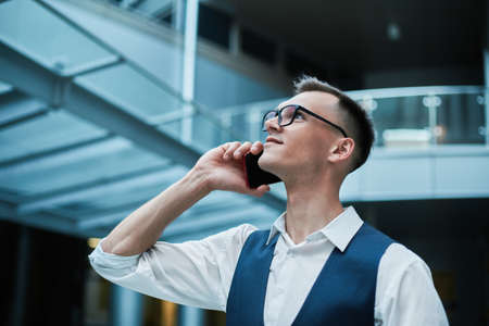 man with a takeaway coffee and a smartphone standing in the lobbの写真素材