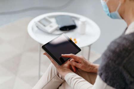 sick woman with a digital tablet sitting on the couch.の写真素材