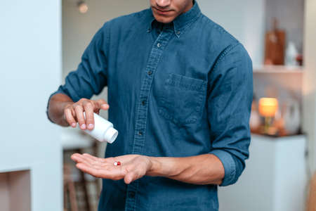 Serious man taking a pill standing at home.の写真素材