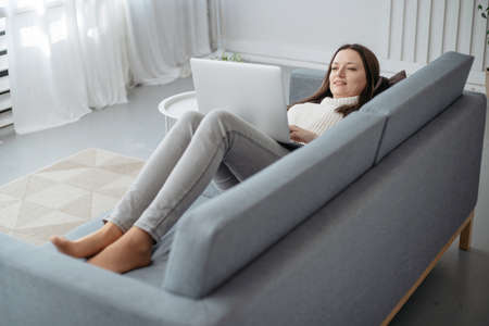 smiling young woman with a laptop lying on the sofa in the living room .の写真素材