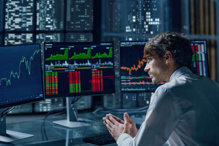 thoughtful young investor looking at his computer monitors .