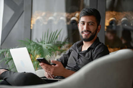 business man with a smartphone and laptop sitting in an armchair .