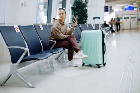 female tourist with a smartphone sitting in the airport waiting room .の写真素材