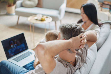 family with children is watching videos on a laptop in their cozy living room .の写真素材