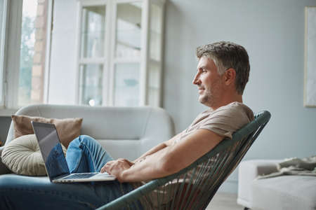 smiling man with a laptop sitting in an armchair .
