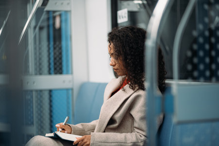 young woman with a pen and notebook sitting in a subway car.の写真素材