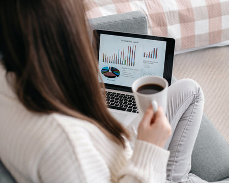 young woman with a laptop is drinking coffee in her bedroom.の写真素材