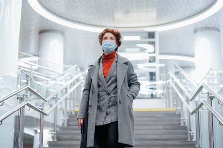 young woman in a protective mask walking down the stairs in the subway.の写真素材