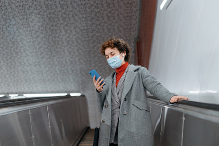 woman in a protective mask standing on the escalator steps in the subway .の写真素材