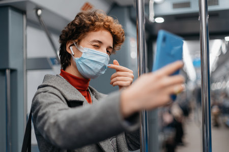 young woman looking at the screen of her smartphone while standing in a subway car.の写真素材