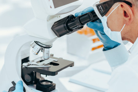 scientist biologist in a protective mask looking through a microscope.の写真素材