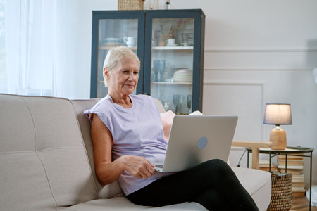 elderly woman with a laptop spends her free time in the living room.