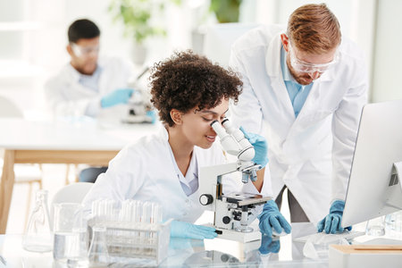 fellow scientists using a computer and a microscope during research.の写真素材