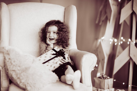 happy cute girl with a Christmas gift sitting in a cozy chair. black and white photoの写真素材